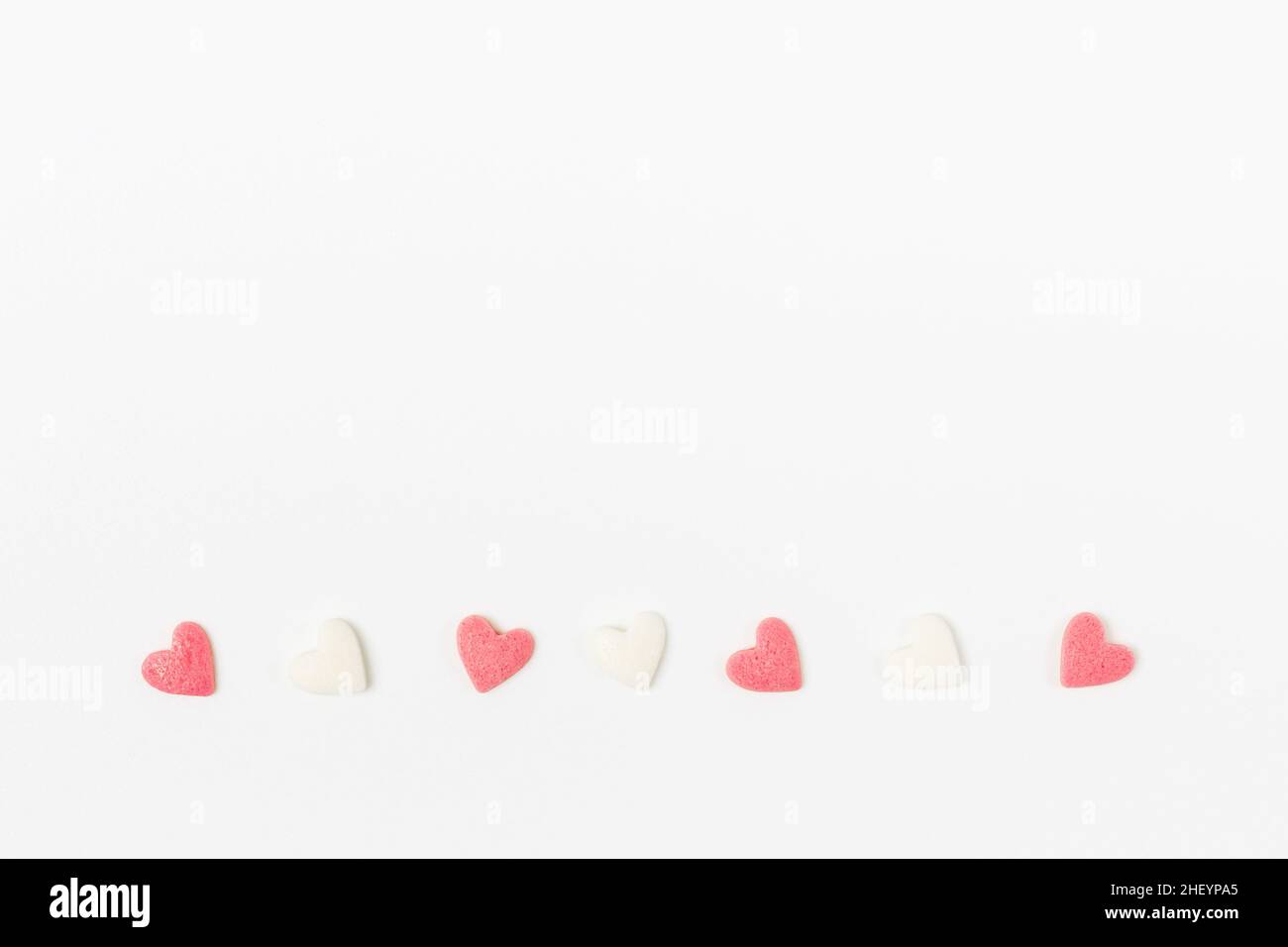 Pink and white heart-shaped sugar candies on white background, minimalistic saint valentine`s day greeting card Stock Photo